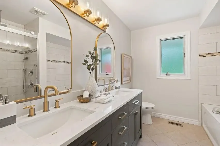 Renovated bathroom with double vanity, brass fixtures and tiled shower