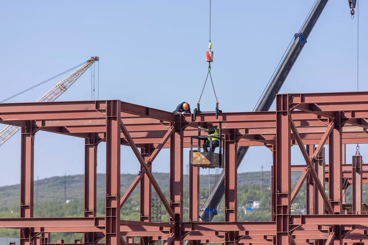 Workers assembling a structural steel building frame with cranes